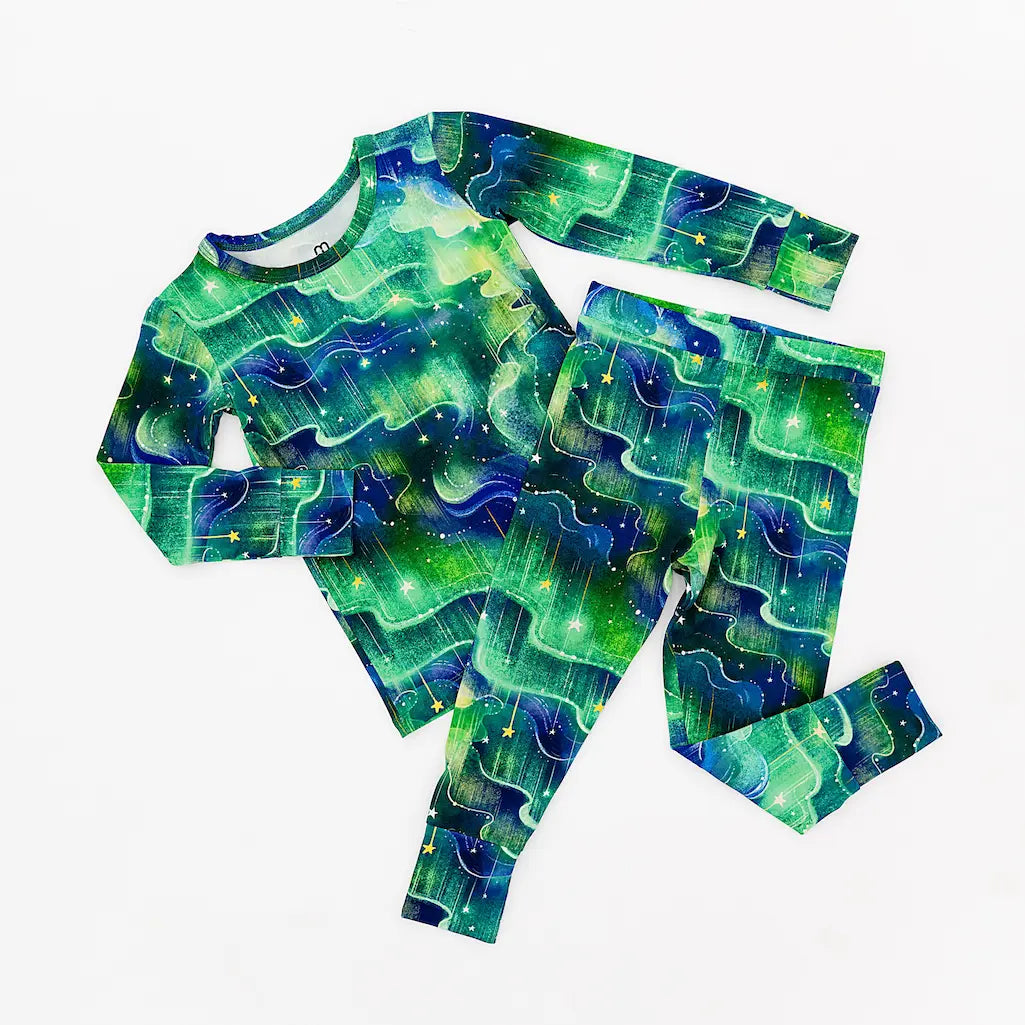 Green and blue long-sleeve shirt and pants pajama set featuring a space-themed pattern with stars and wavy lines, displayed on a white background