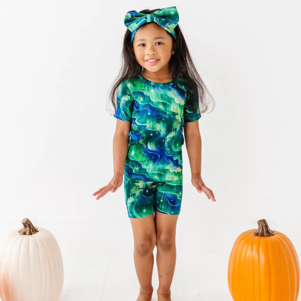 Child wearing a green and blue patterned outfit with pumpkins on a white background