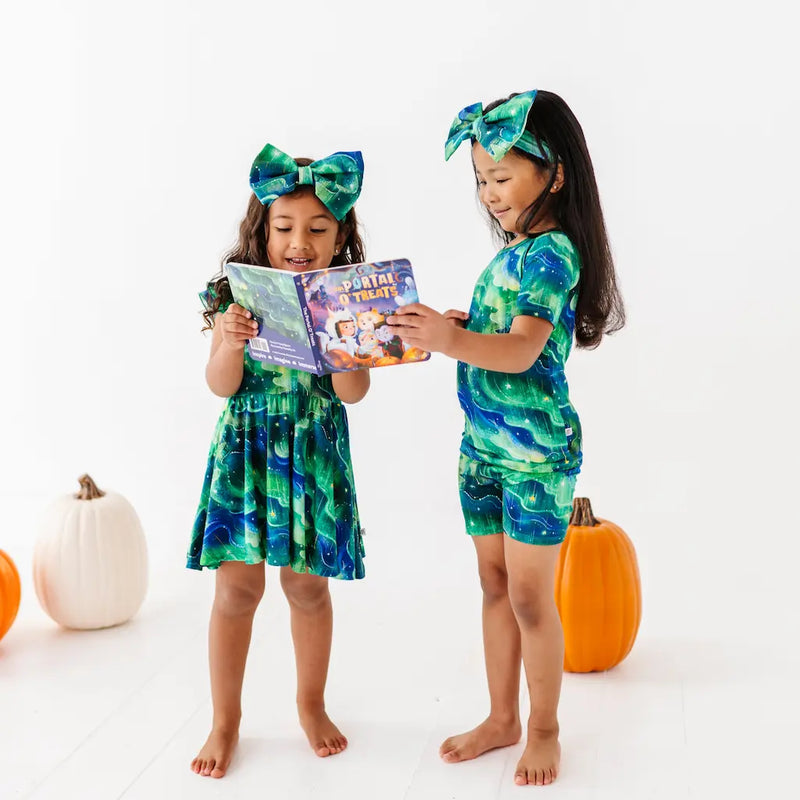 Two children in matching green and blue outfits with pumpkins on a white background
