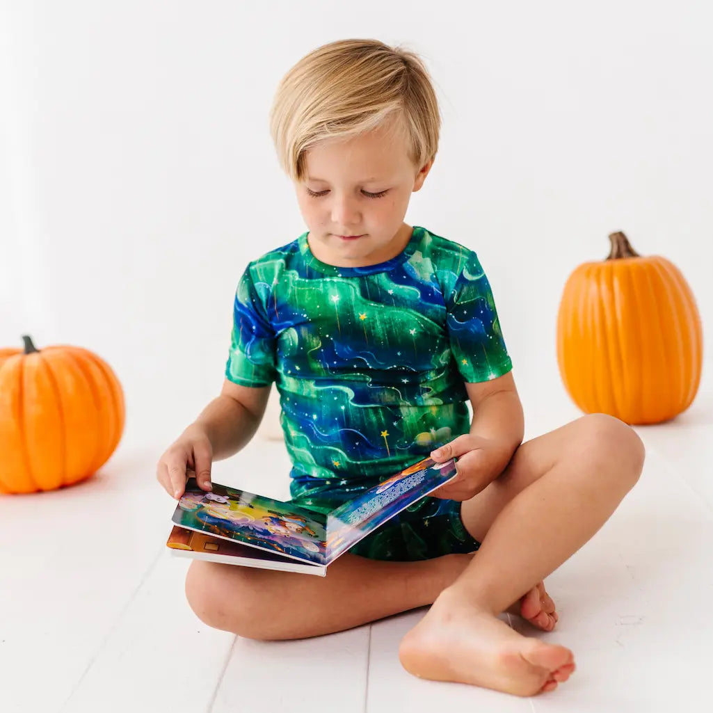 Child wearing a green and blue shirt with pumpkins on a white floor