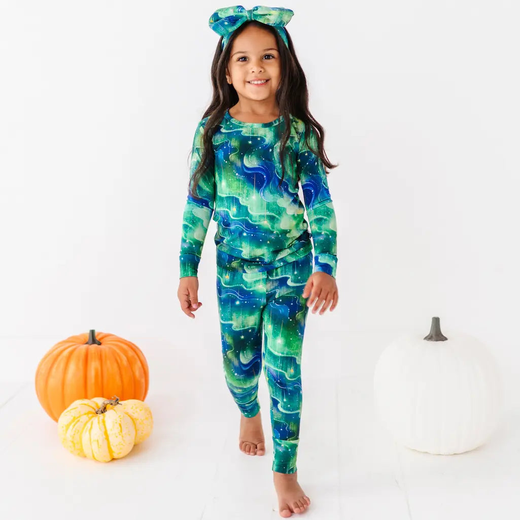 Child wearing a green and blue patterned onesie with pumpkins on a white background
