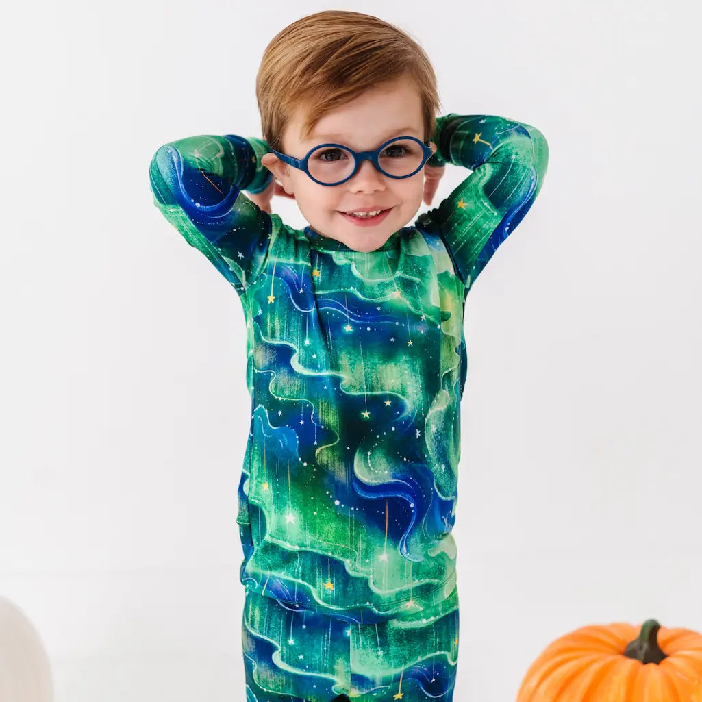 Child wearing a green and blue galaxy-themed onesie with a pumpkin in the background.