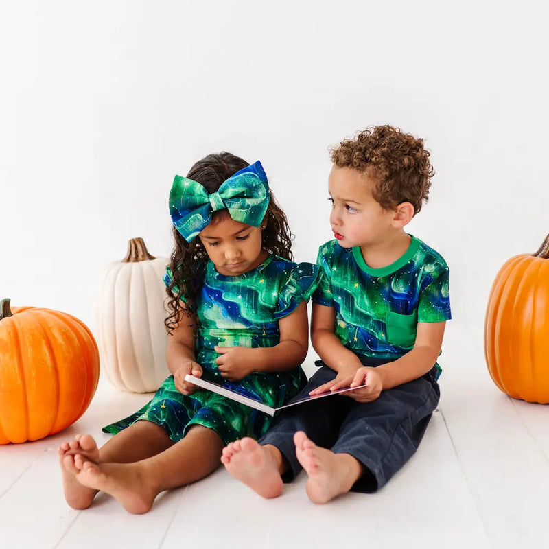 Two children in matching green and blue outfits with pumpkins on a white background