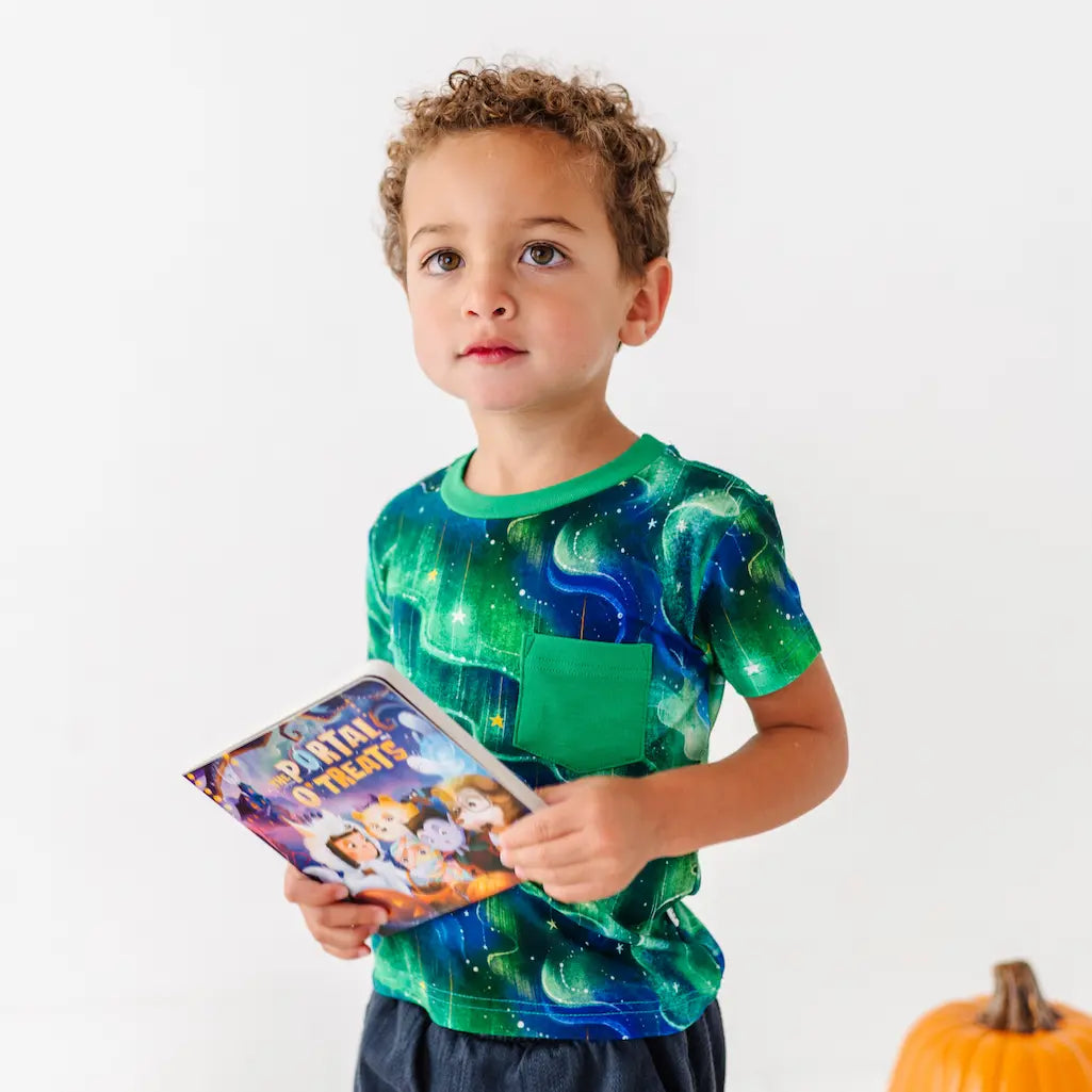 Child wearing a green space-themed shirt holding a book with a white background