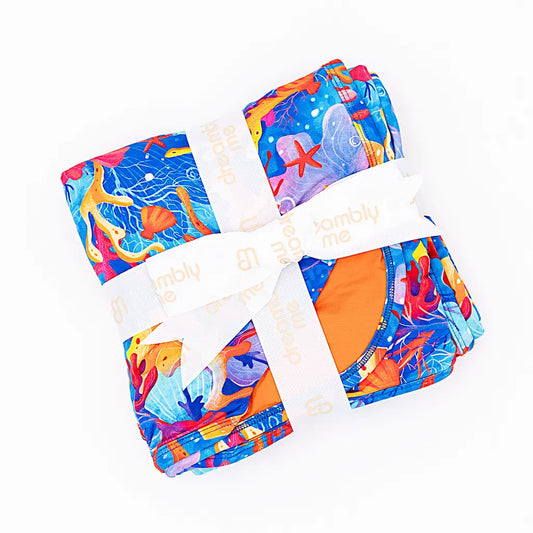 A folded blanket with a vibrant underwater coral and sea life pattern, tied with a white ribbon.