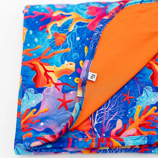 A folded blanket with a vibrant coral, starfish, and sea plant pattern in shades of blue, orange, and purple, with a solid orange underside visible at one end.