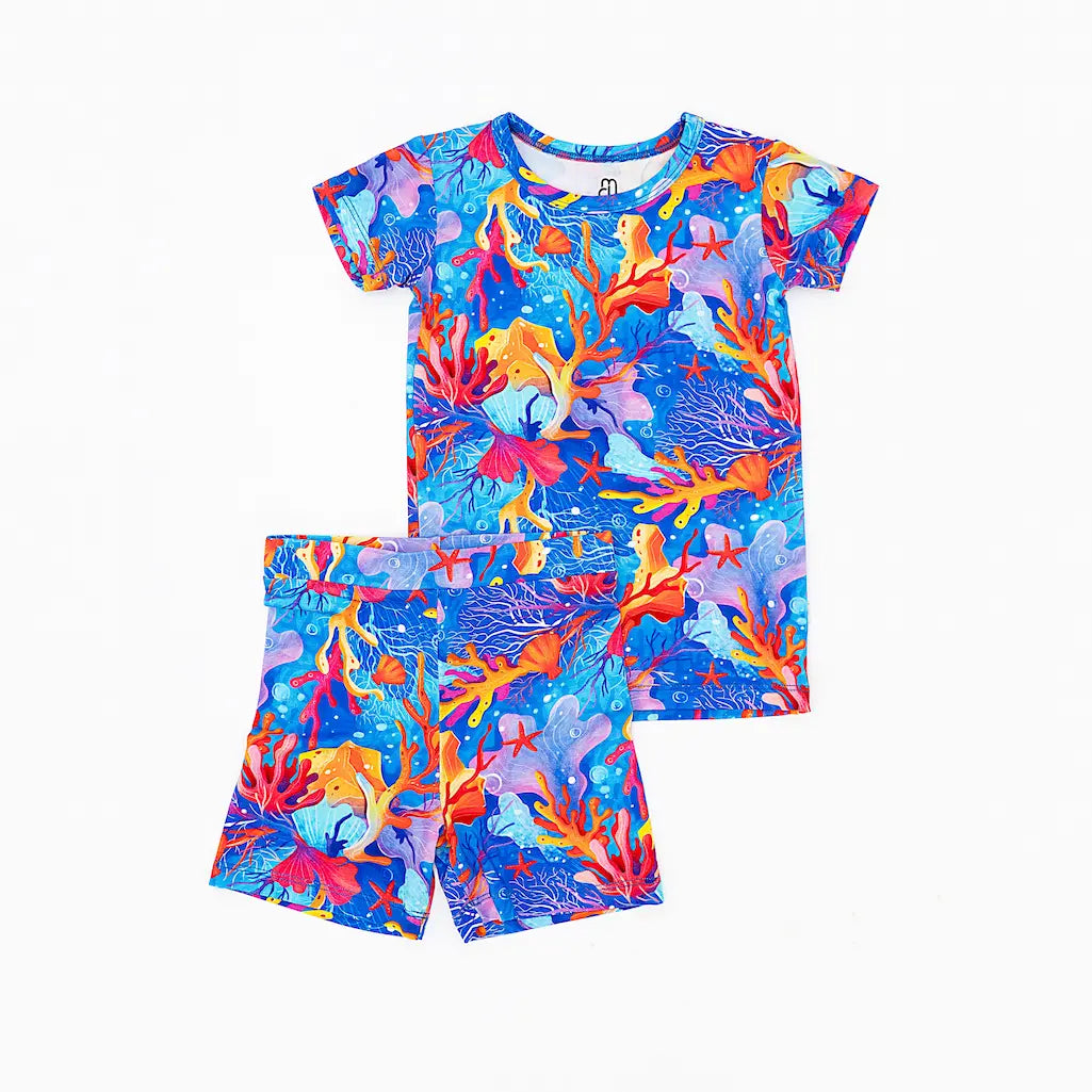 A short pajama set for children with a vibrant coral and sea life pattern in shades of blue, orange, and purple.