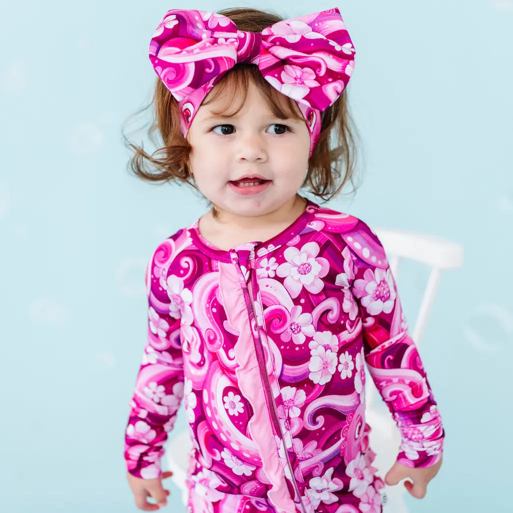 Child wearing a pink and purple patterned outfit with a matching headband against a light blue background.