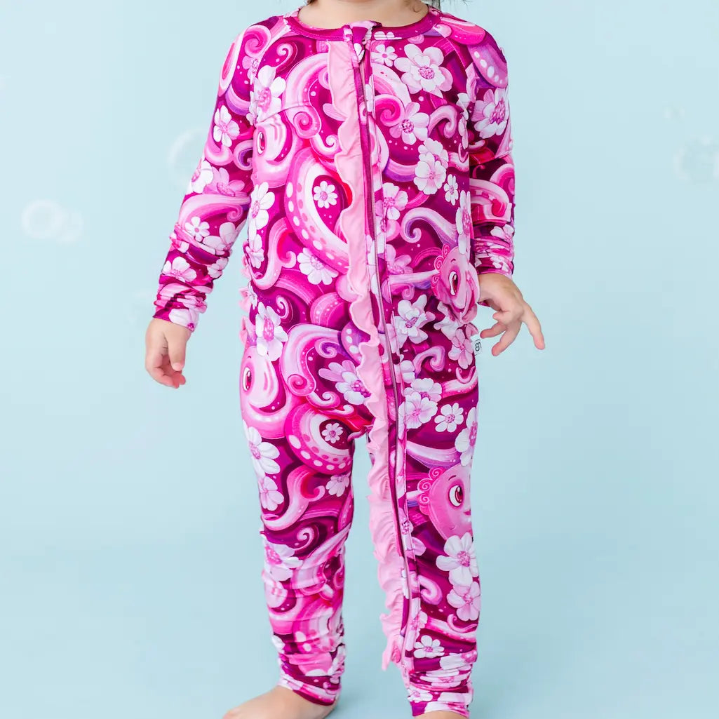 Child wearing a pink and white patterned onesie on a light blue background