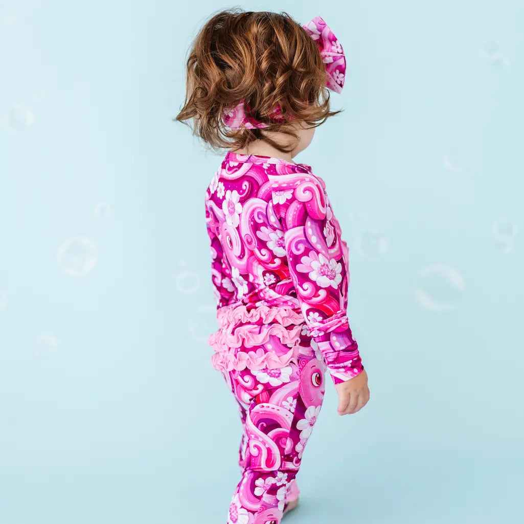 Child wearing a pink and purple patterned outfit on a light blue background.