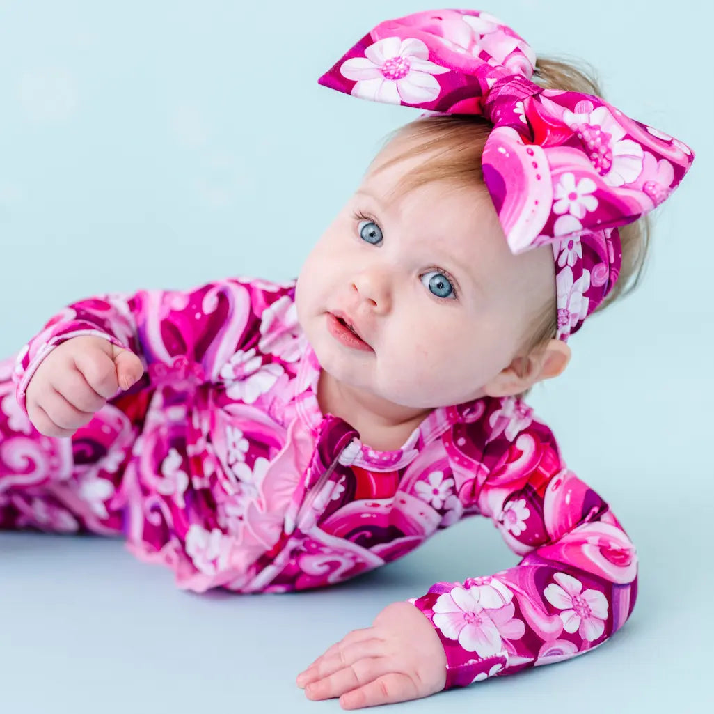 Baby in pink floral outfit with matching headband on a light blue background