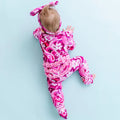 A baby wearing a pink ruffle pajama with a pattern of swirling tentacles and flowers, lying on a light blue background.