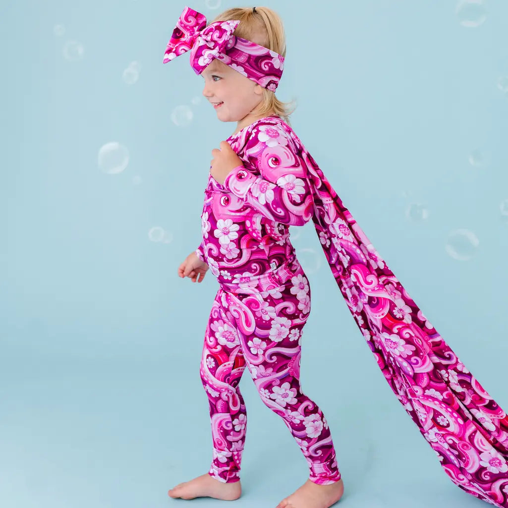 A child wearing a pink octopus-themed pajama set with a bow on the head, standing against a blue background with bubbles around.