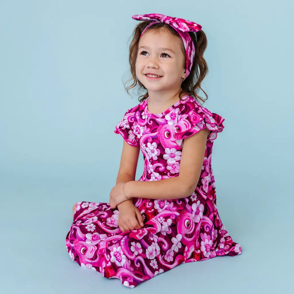 Young girl wearing a pink and purple floral dress with a matching headband against a light blue background
