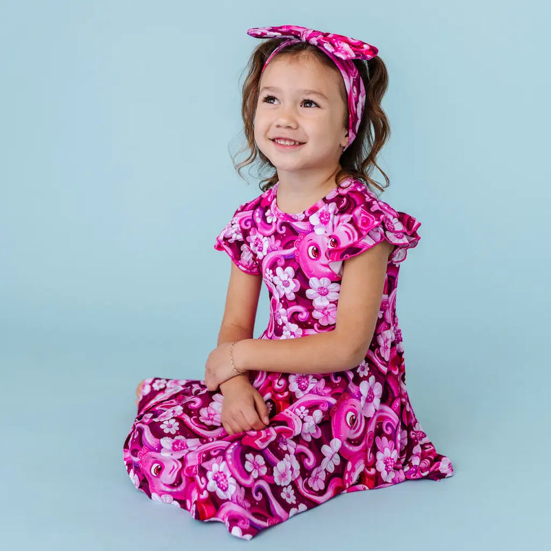 Young girl wearing a pink and purple floral dress with a matching headband against a light blue background