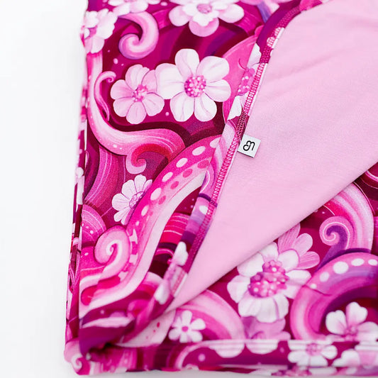 A close-up of a pink pajama blanket with a floral and octopus pattern, showing a small octopus character and a label.