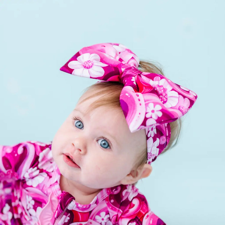 A baby wearing a pink headband with a pattern of swirling tentacles and white flowers.