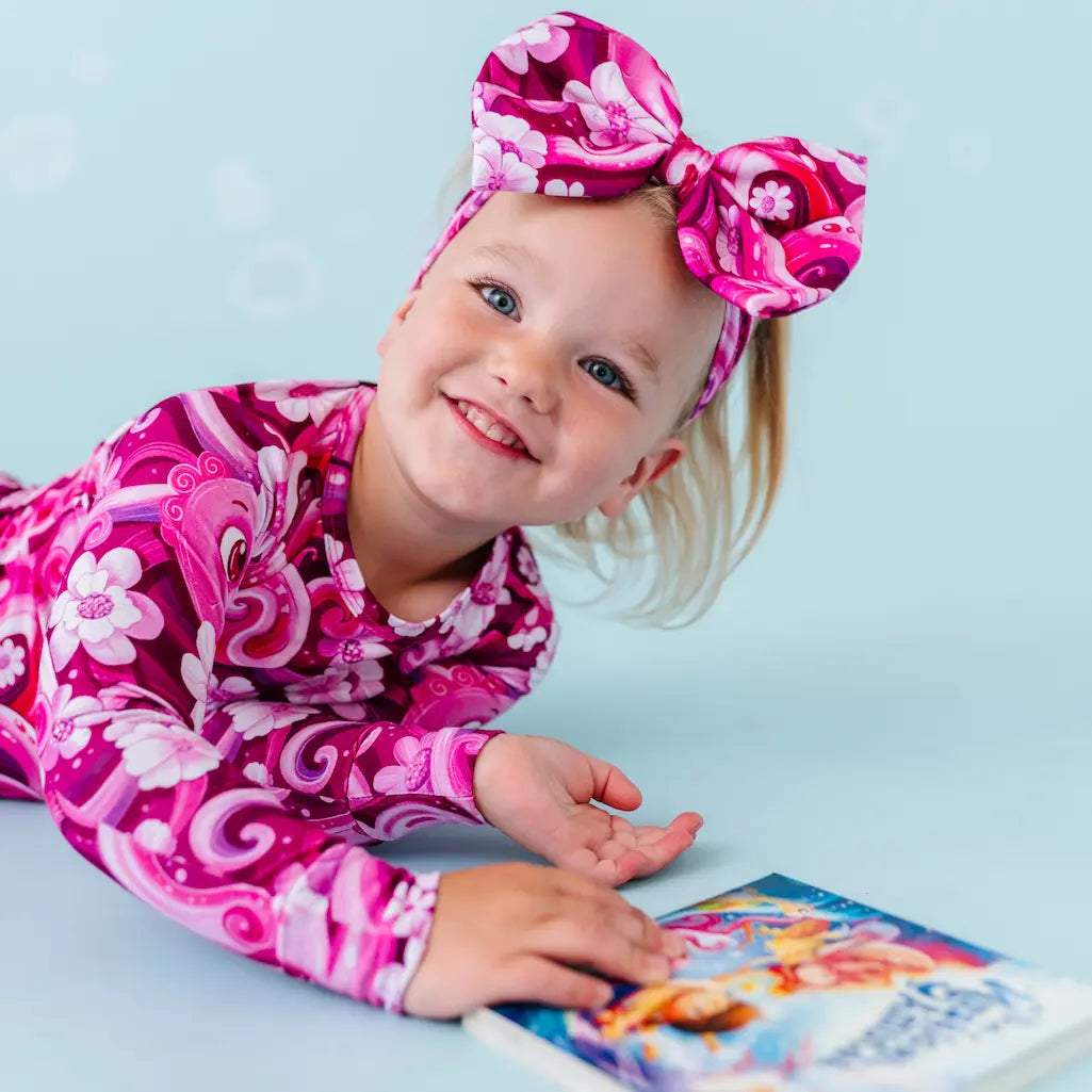 Young girl in pink floral outfit with headband on a light blue background