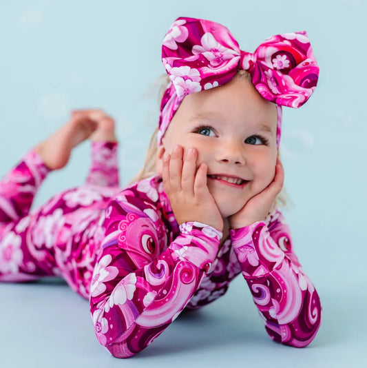A young child wearing a pink pajama set with a floral and octopus design, matching bow on head.