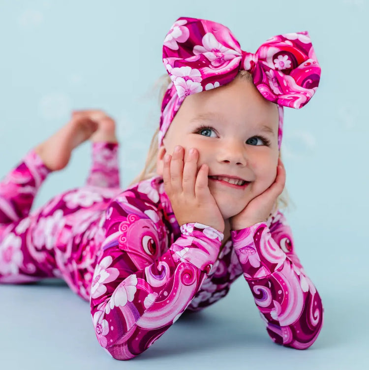 A young child wearing a pink pajama set with a floral and octopus design, matching bow on head.