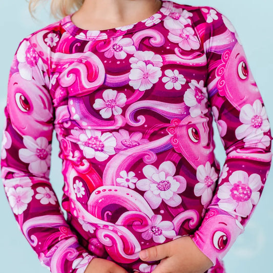 Child wearing a pink and purple patterned shirt with fish and floral designs on a light blue background