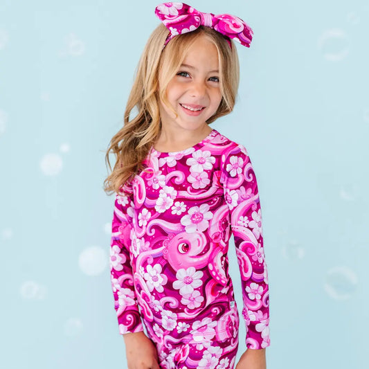 Young girl wearing a pink and purple dress with floral patterns on a blue background.