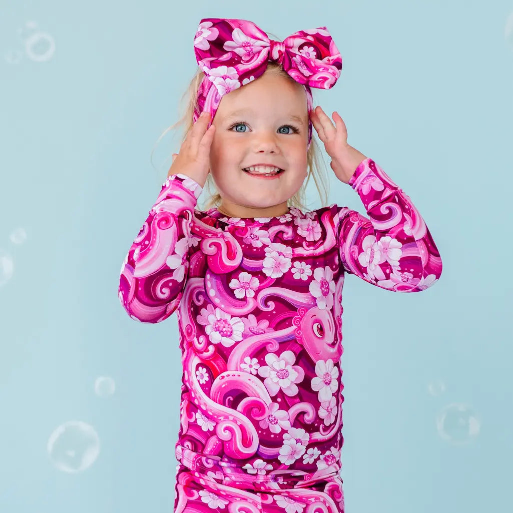 Child wearing a pink and purple swimsuit with a bow on a blue background.
