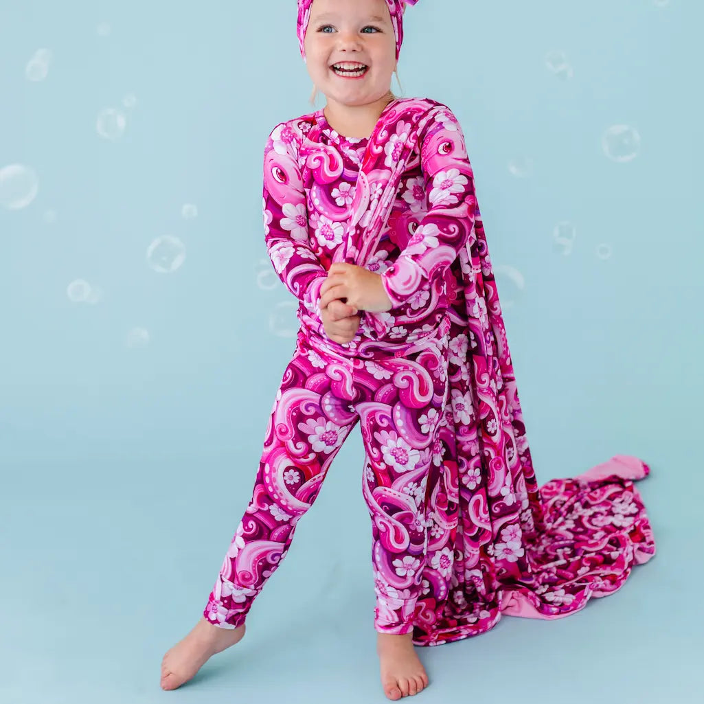Child wearing a pink and purple patterned onesie on a blue background.