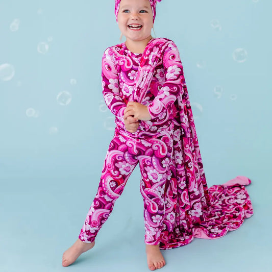 Child wearing a pink and purple patterned onesie on a blue background.