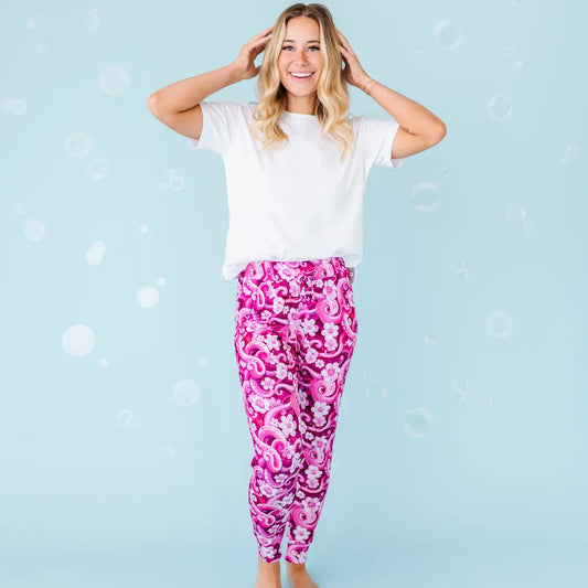 A woman standing and posing with her hands on her head, wearing white and pink patterned pajama pants with a white t-shirt