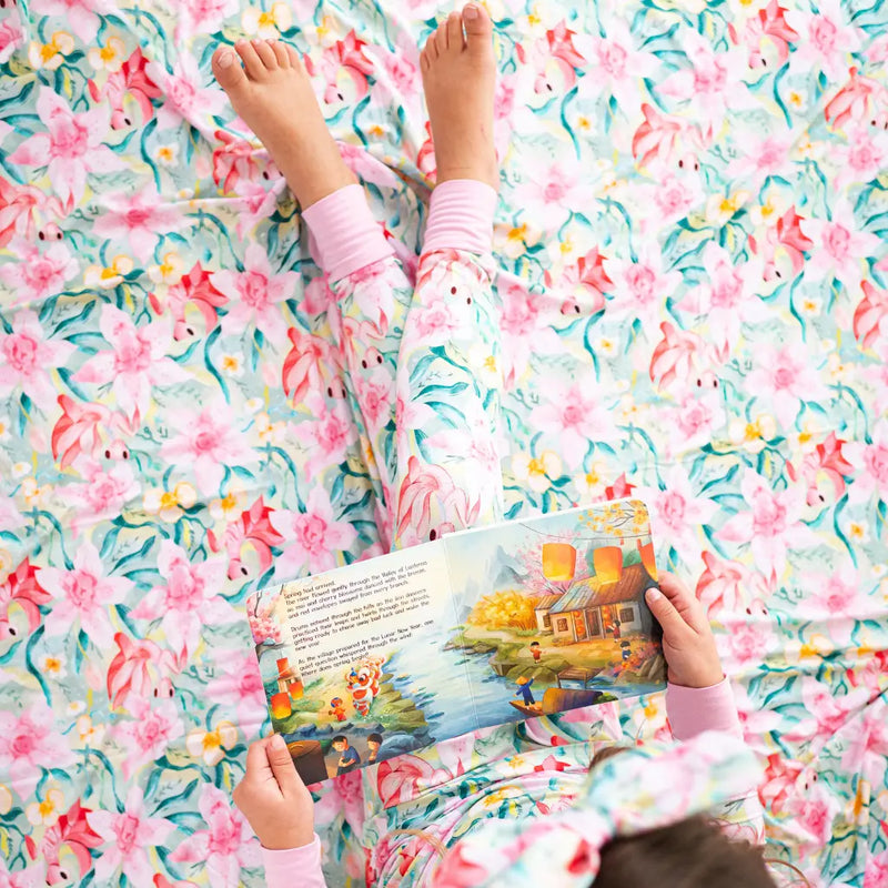 Child reading a book on a floral-patterned blanket