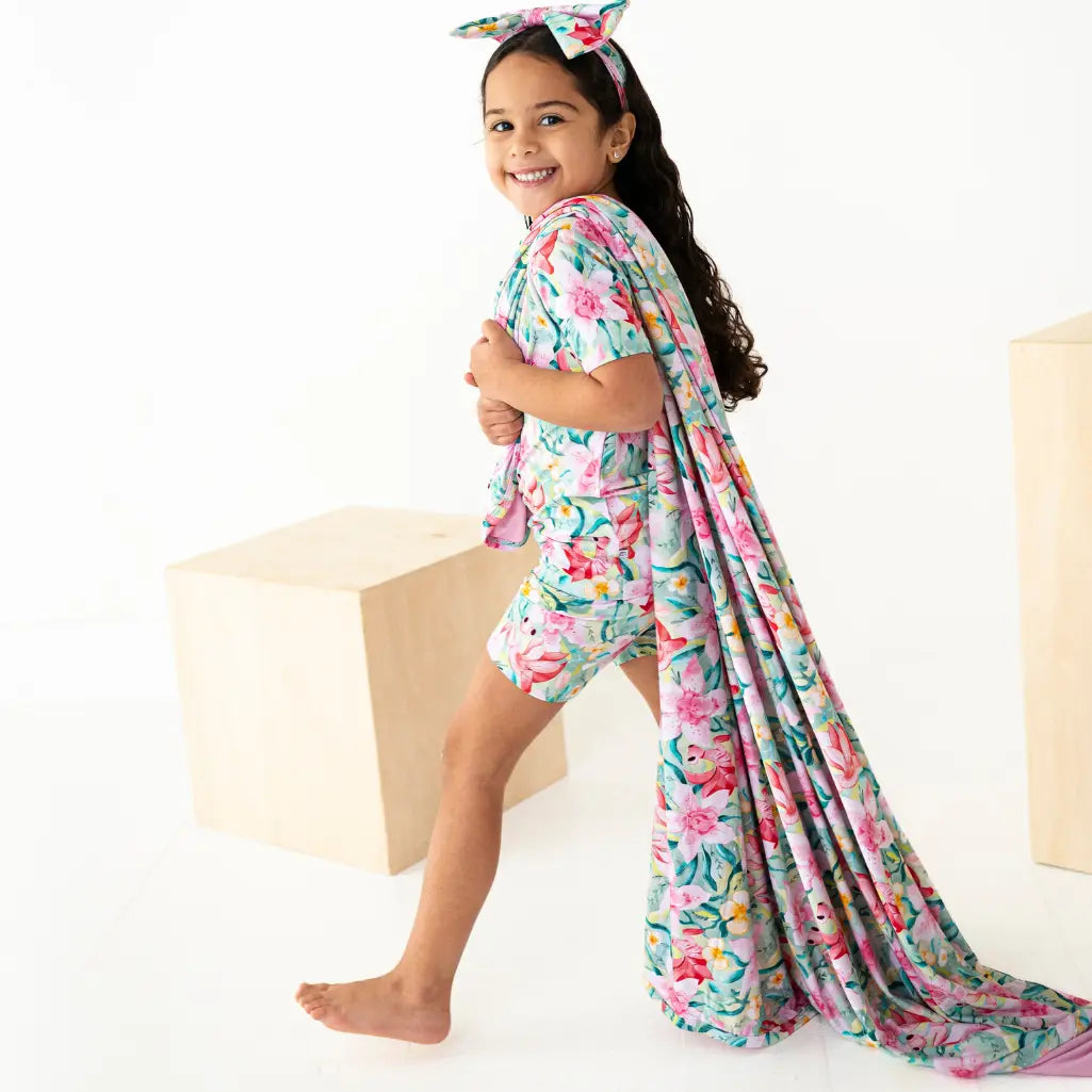 Young girl wearing a floral dress and headband, standing against a white background