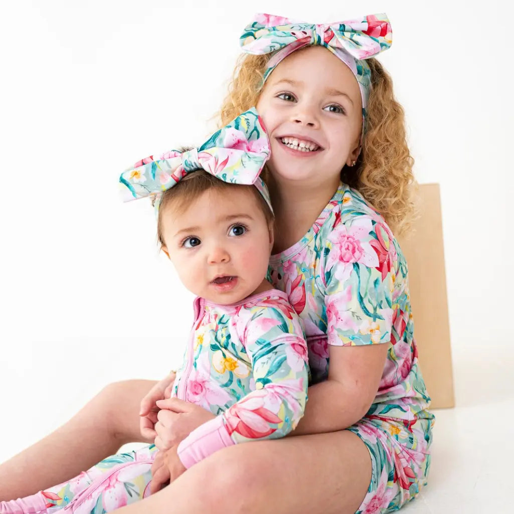 Two children wearing floral outfits with matching headbands on a white background