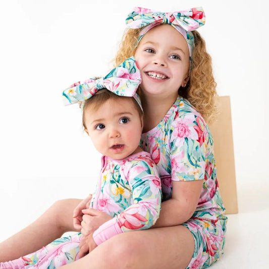 Two children wearing floral outfits with matching headbands on a white background