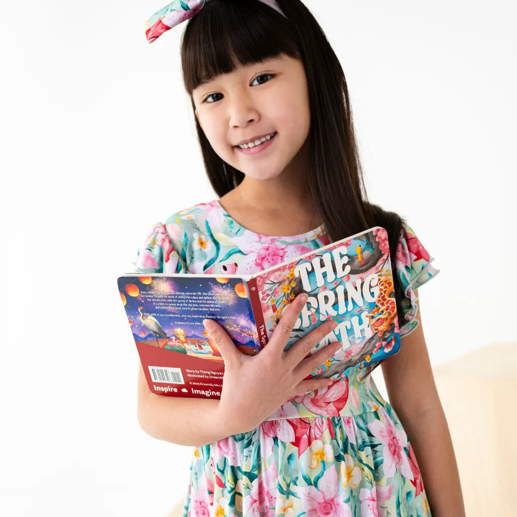 Young girl in a floral dress holding a book titled 'The Spring' on a white background
