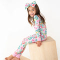 Young girl wearing a floral onesie and headband sitting on a wooden block against a white background