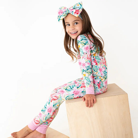 Young girl wearing a floral onesie and headband sitting on a wooden block against a white background