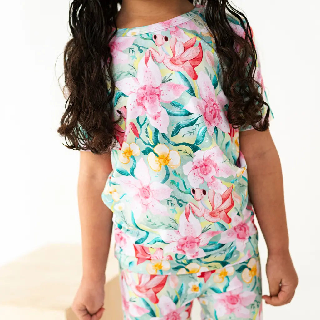 Child wearing a floral dress with pink flowers and green leaves on a white background