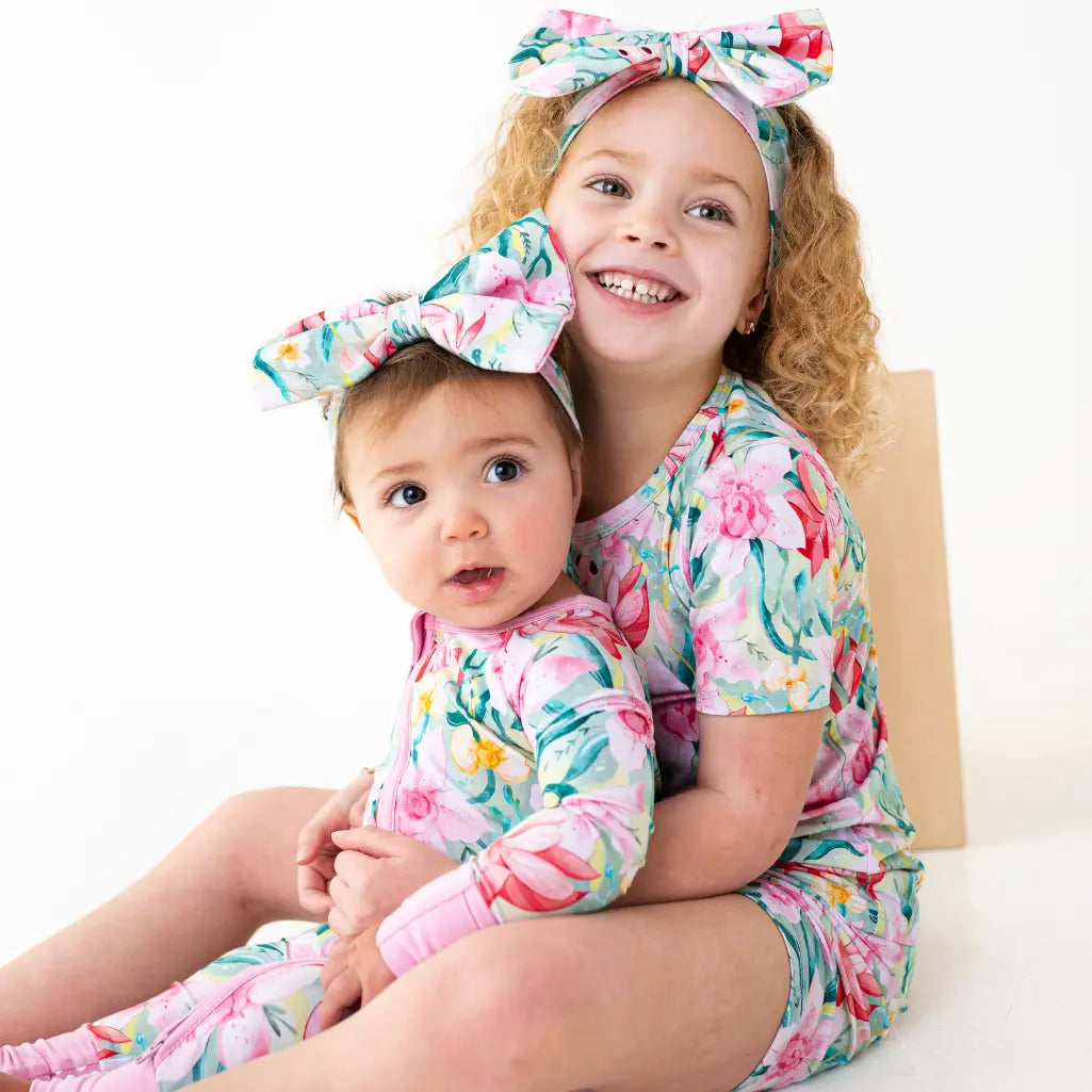 Two children wearing matching floral outfits with headbands on a white background