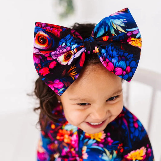 A child wearing a colorful floral bow headband with a pattern of owls and forest plants.