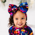 A child wearing a colorful floral dress and a matching bowtiful headband with a pattern of owls and forest plants.