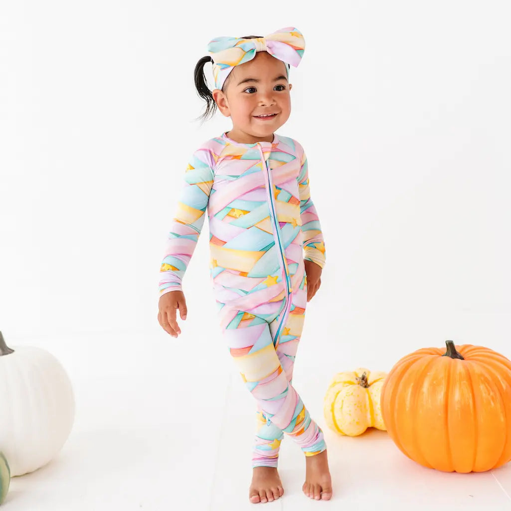 Child wearing a colorful striped onesie with pumpkins on a white background