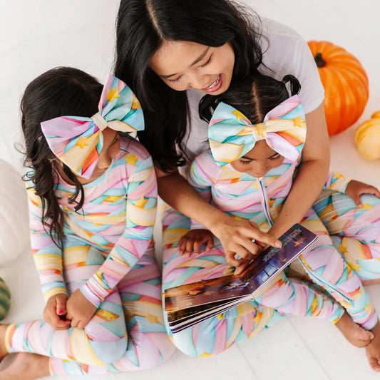 Two children in colorful outfits with large bows reading a book, surrounded by pumpkins.