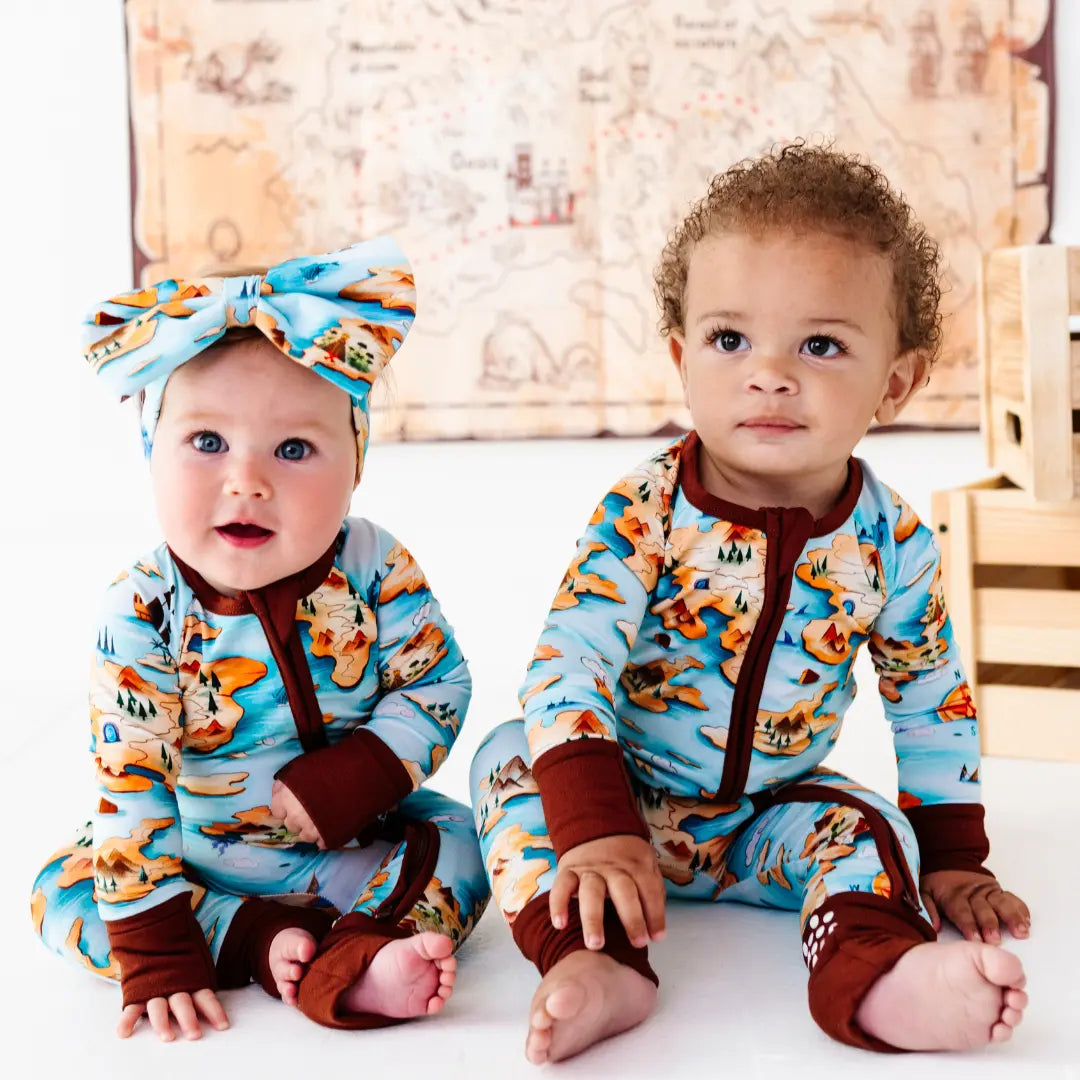 Two babies wearing matching outfits with a fox pattern in a wooden room.