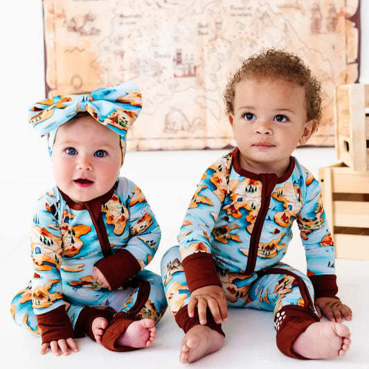 Two babies wearing matching outfits with a fox pattern in a wooden room.