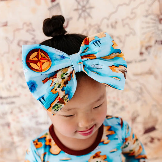 Child wearing a large blue bow with cartoon character design on a neutral background