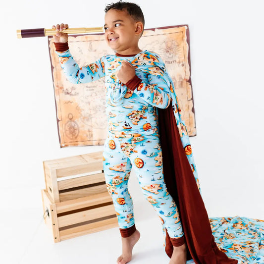 Child wearing a superhero costume with a cape and mask, standing in front of a wooden crate and map.