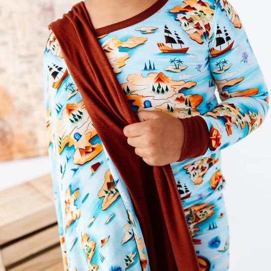 Person wearing a colorful shirt with a ship and landscape pattern, holding a brown scarf.