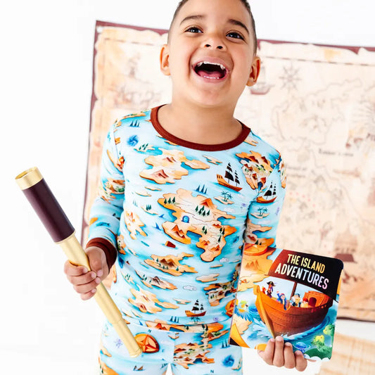 Child wearing a pajama set with island adventure design, holding a wooden paddle and book.