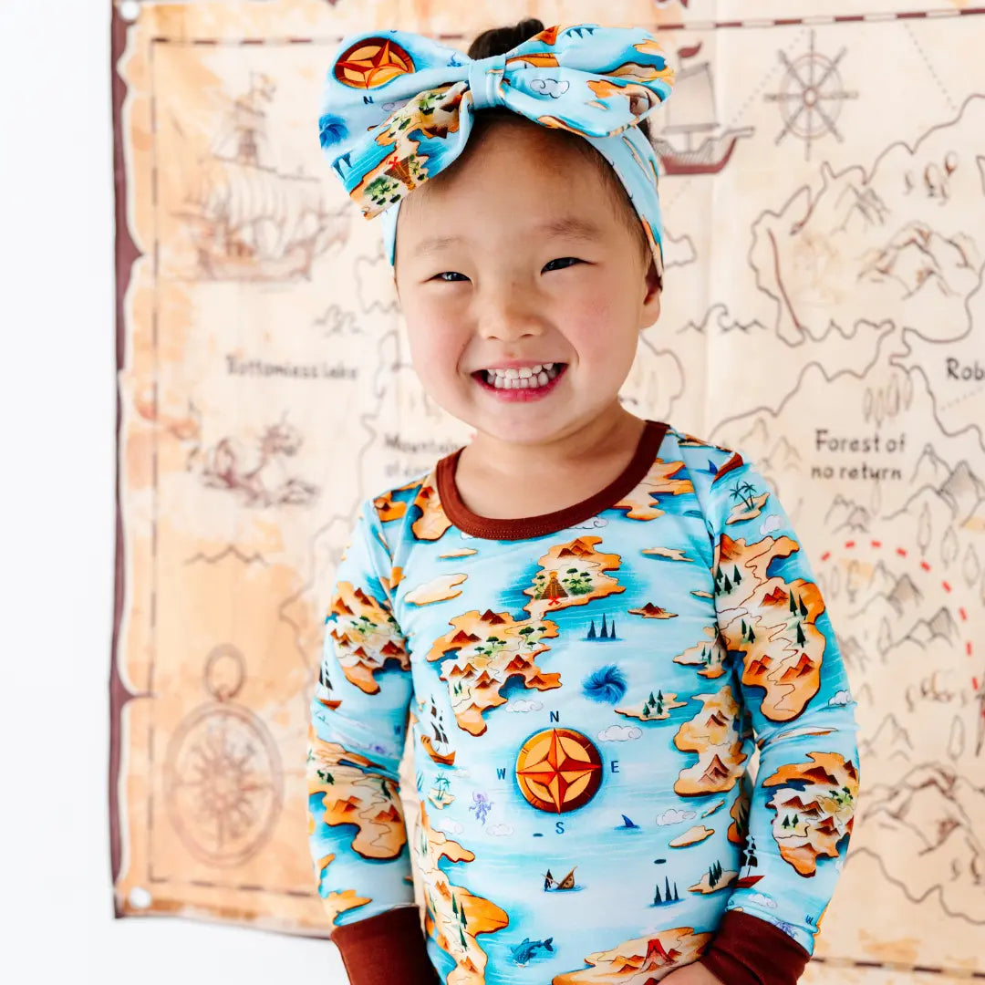 Child wearing a colorful map-themed shirt and headband, standing in front of a decorative map background.
